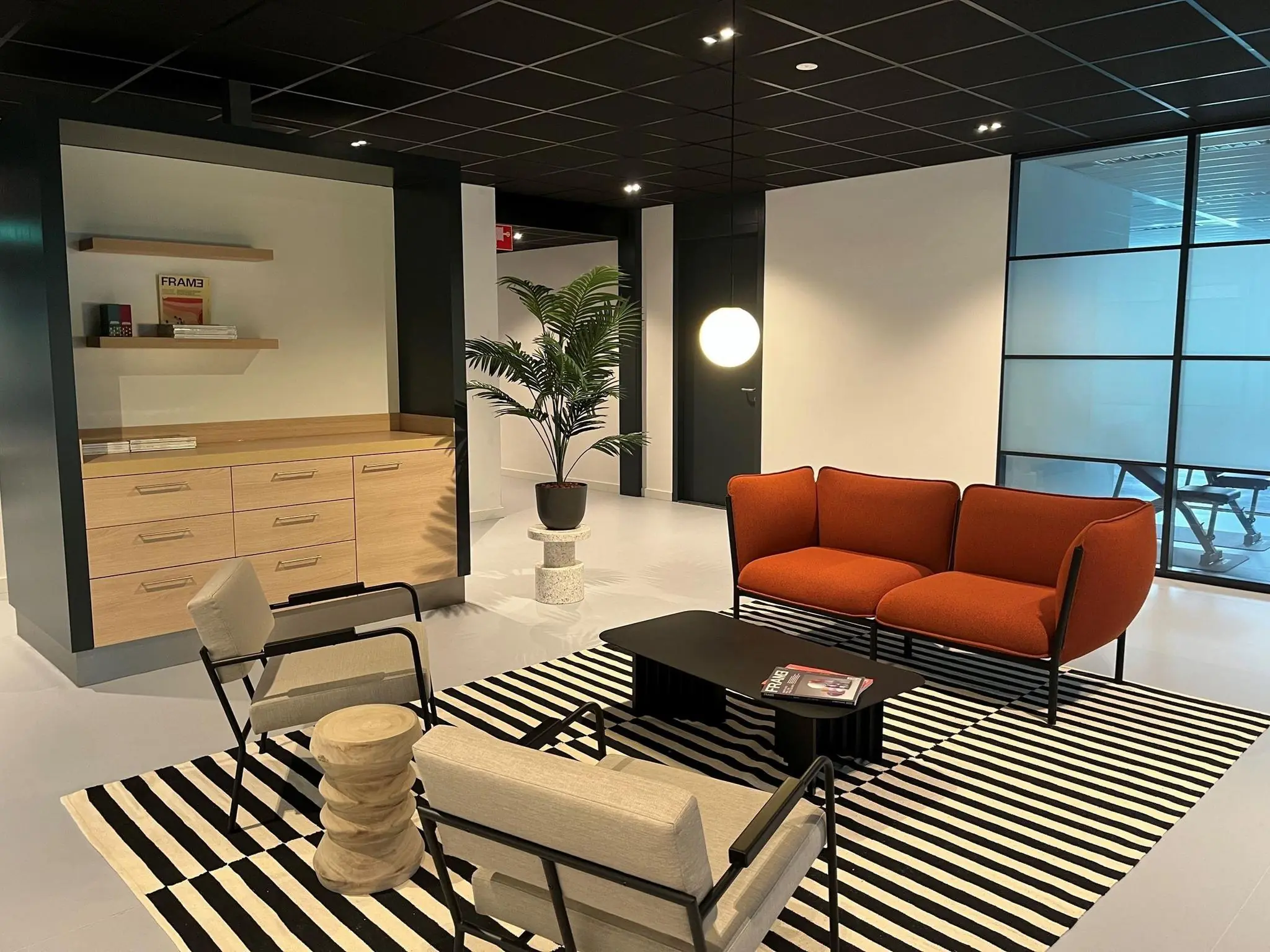 Moderne wachtruimte met een oranje bank, zwart-wit gestreept vloerkleed en minimalistische inrichting.